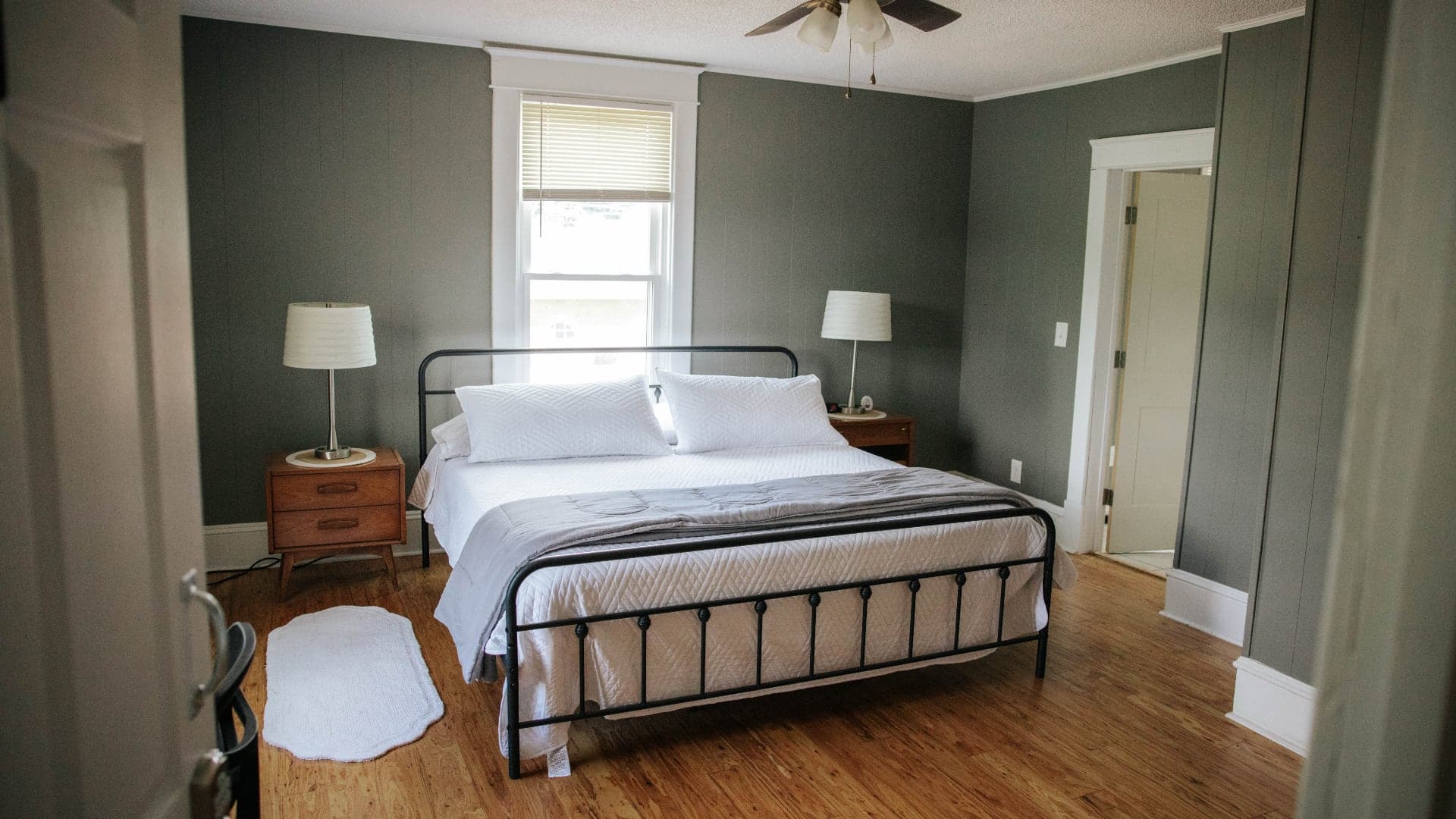 A cozy bedroom featuring a metal bed frame, white linens, wooden flooring, and soft lighting.
