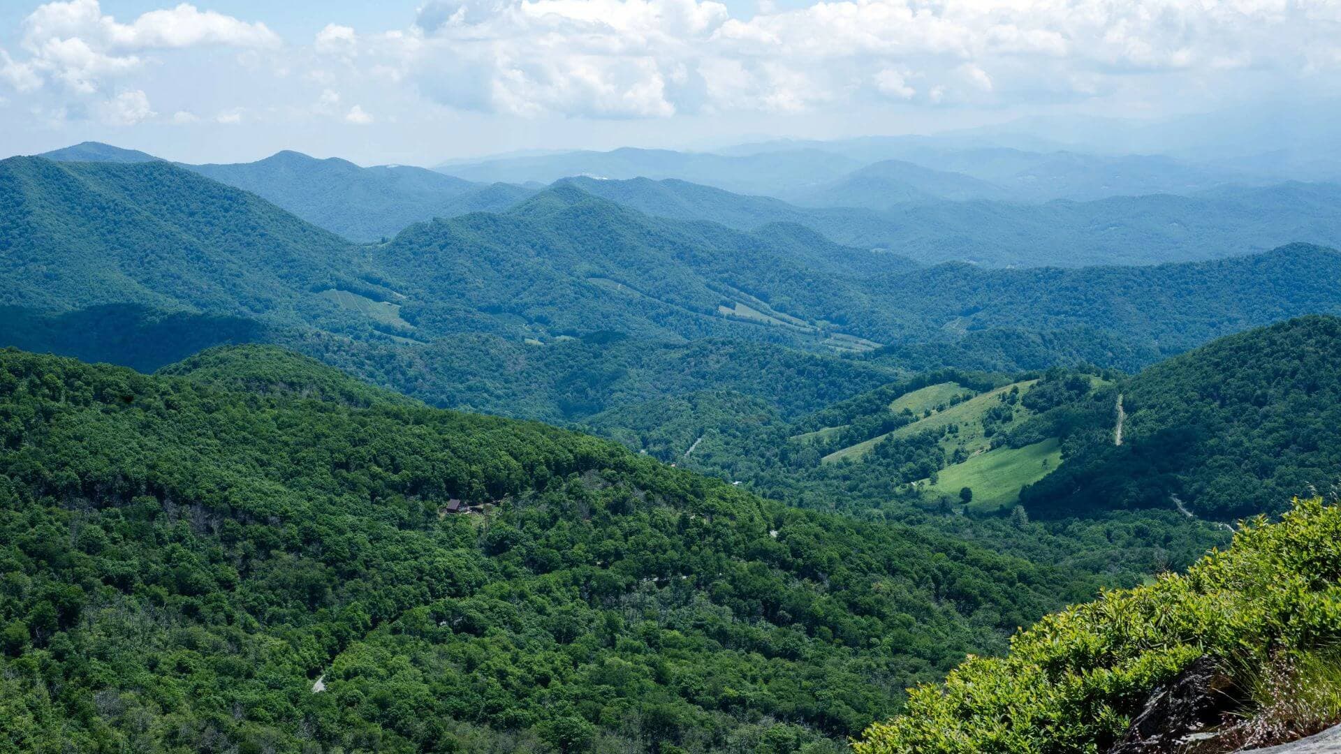 A panoramic view of green mountain ranges under a partly cloudy sky.